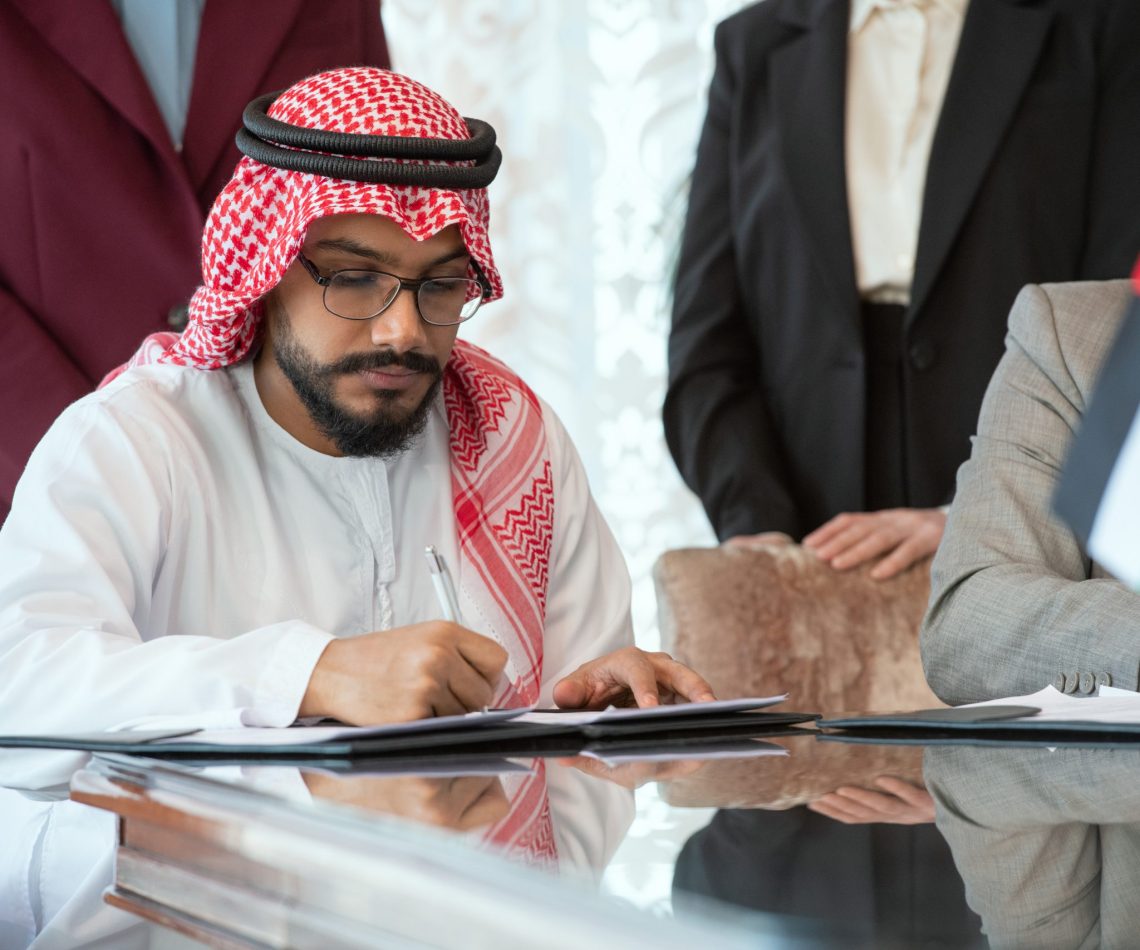 Confident Arabian businessman or delegate in national clothes signing contract