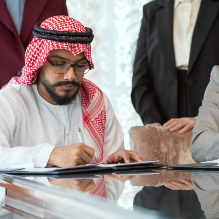 Confident Arabian businessman or delegate in national clothes signing contract