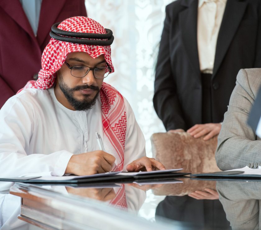 Confident Arabian businessman or delegate in national clothes signing contract